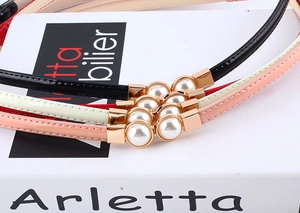 Detail of slim patent leather belts with elegant double pearl and gold buckles