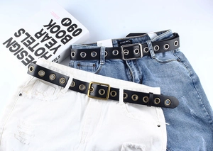 Vue détaillée des ceintures en similicuir noir avec œillets métalliques sur jeans en denim