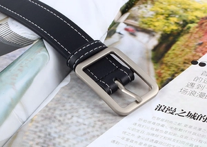 Détail d'une ceinture en cuir noir avec surpiqûres blanches et boucle carrée en argent mat