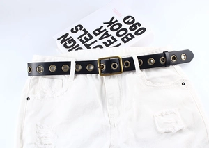 Détail de la ceinture à œillets noirs avec rivets dorés sur short en jean blanc