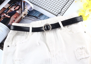 Détail d'une ceinture noire en similicuir avec boucle ronde argentée sur un short en jean