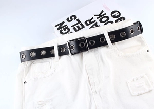 Détail de la ceinture noire en similicuir avec œillets argentés sur un short en jean