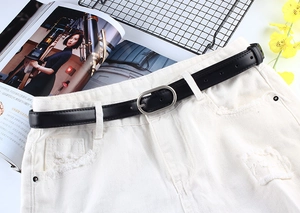 Détail de ceinture noire en simili cuir avec boucle ovale argentée sur un jean blanc