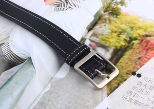 Détail de ceinture en cuir noir avec surpiqûres blanches et boucle carrée en métal mat