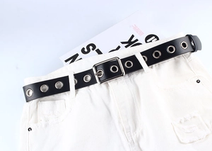 Détail d'une ceinture en cuir PU noir avec œillets argentés et boucle sur un jean blanc