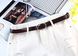 Ceinture fine marron avec boucle ovale argentée sur un jean blanc déchiré
