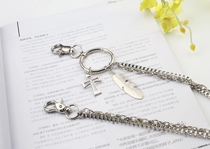 Detail of silver metal waist chain with cross and feather pendants on a fashion magazine