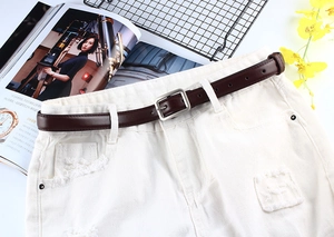 Détail d'une fine ceinture marron foncé avec boucle carrée argentée sur un jean