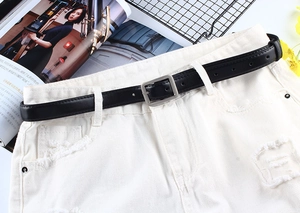 Détail d'une ceinture fine en cuir PU noir avec boucle argentée sur un jean blanc
