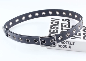 Détail d'une ceinture noire en PU avec œillets métalliques argentés et boucle carrée ardillon