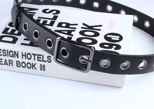 Détail d'une ceinture noire en PU avec œillets métalliques argentés et boucle carrée