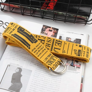 Close-up of yellow canvas belt with black letter print and metal double D-ring buckle