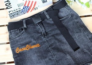 Close-up of dark gray denim skirt with orange CocoChance embroidery and black belt