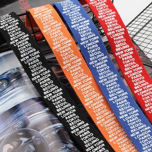 Long woven canvas belts in black, orange, blue, and red with city name jacquard patterns