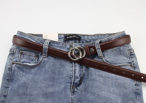 Detail of slim dark brown leather belt with silver double ring buckle on blue jeans
