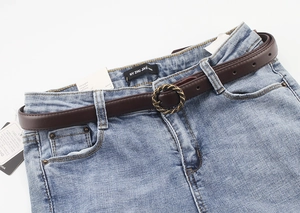 Détail d'une boucle ronde torsadée rétro sur une ceinture fine marron avec un jean bleu