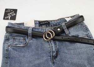 Detail view of a black slim leather belt with a golden double ring buckle on blue jeans