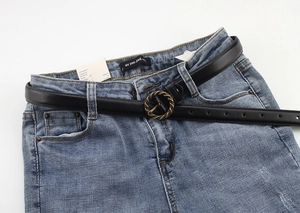 Détail d'une ceinture fine en cuir noir avec boucle ronde en métal tressé sur jean
