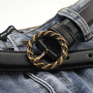 Ceinture fine en cuir noir vintage avec boucle ronde torsadée en bronze sur un jean bleu