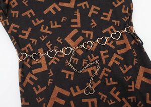 Detail of a golden heart-shaped metal link waist chain with extender on a dark garment