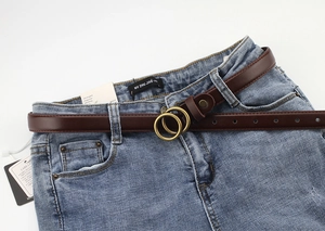 Close-up of retro dark brown leather thin belt with bronze double ring buckle on jeans