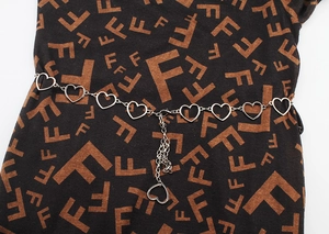 Close-up of silver metal chain belt featuring hollow heart links and a hanging heart charm