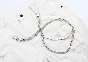 Détail de la chaîne de pantalon double couche en métal argenté sur un jean blanc usé