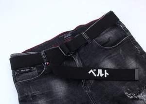 Détail d'un jean denim noir vieilli avec une ceinture en toile imprimée et boucle à double anneau