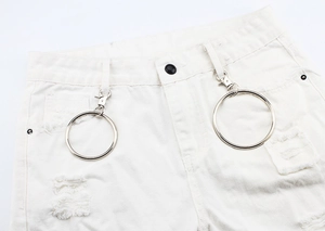 Détail d'un jean blanc avec des anneaux en métal argenté et des bords effilochés punk