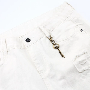 Detailed close-up of a vintage bronze metal key pendant on white denim jeans fabric