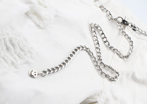 Gros plan d'une chaîne de taille argentée avec pendentif smiley ajouré sur un jean blanc