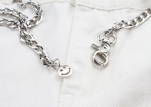 Détail d'une chaîne de pantalon en métal argenté avec mousqueton et pendentif smiley