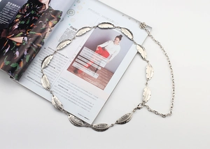 Detail of silver leaf metal chain belt with feather charms and rose clasp on white background
