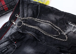 Detail of silver double-layered metal trousers chain styled on black distressed jeans