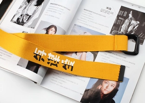 Detailed shot of yellow canvas belt with black double D-ring buckle and printed text