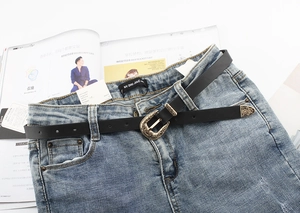 Close-up of black thin leather belt with vintage floral engraved gold buckle on denim jeans