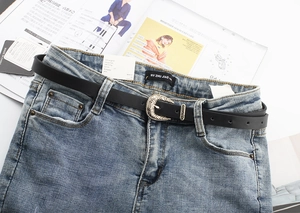Close-up of a slim black leather belt with an engraved silver buckle on denim jeans