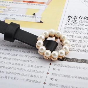 Close-up of elegant pearl-encrusted circular buckle on a slim black leather waist belt