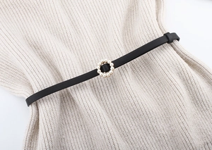 Detail of elegant black slim belt with a round pearl buckle on beige knit fabric