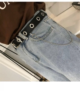 Detail of black punk leather belt with silver grommets and chain on blue denim jeans