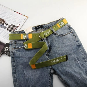 Green canvas belt with double D-rings and orange print styling on dark blue jeans