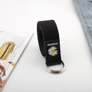 Détail d'une ceinture en toile noire avec double boucle D et écusson marguerite blanche