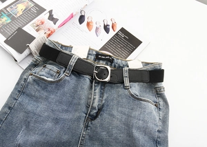 Détail d'une ceinture tressée élastique noire avec boucle argentée sur un jean bleu