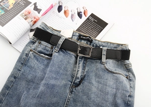 Détail d'une ceinture tressée élastique noire avec boucle argentée sur un jean