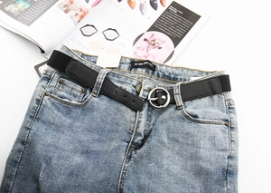 Détail de la ceinture élastique tressée noire avec boucle ronde argentée sur un jean