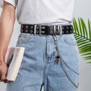 Detail of black punk belt with double silver grommets and astronaut chain on blue jeans