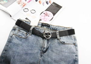 Détail d'une ceinture élastique noire avec boucle coeur argentée sur un jean bleu clair