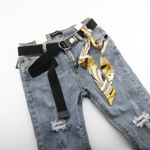Détail d'un jean bleu clair déchiré avec ceinture en toile noire et foulard en soie à motif