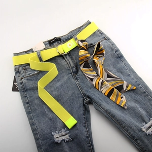 Détail d'une ceinture en toile jaune à marguerites avec foulard et jean délavé