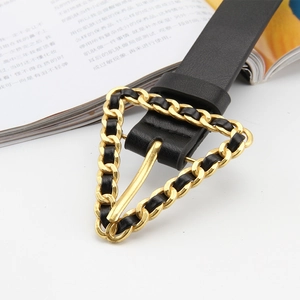 Détail de la ceinture en cuir noir avec une boucle triangulaire dorée et maillons de chaîne